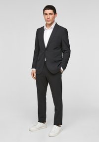 Donker op maat gemaakt pak met een enkele knoop, gecombineerd met een wit overhemd en witte sneakers. Gladde stof, slim fit en minimalistisch ontwerp.