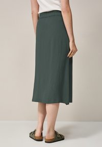 Groene, knielange rok van een gestructureerde stof, met een elastische tailleband en een relaxed fit. Gepaard met platte instapschoenen met strikken.