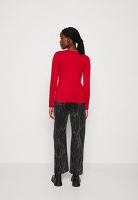 Maglietta rossa a maniche lunghe aderente abbinata a pantaloni neri larghi con motivo marmorizzato. L'outfit è completato da stivaletti neri alla caviglia.