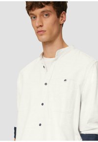 Witte, gestructureerde shirt met een bandkraag, voorzien van donkere knopen en een borstzak. De mouwen hebben marineblauwe accenten.