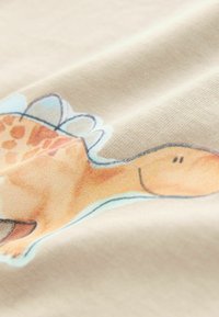 Beež puuvillakangas, millel on trükitud dinosauruse disain ja sinine õhkkant. Sile tekstuur kerge venivusega.