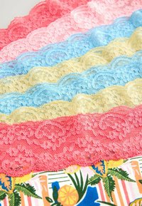 Sorok finom csipkefonatból rózsaszín, világos rózsaszín, kék, sárga, kék, sárga és korall színekben, színes virágos és csíkozott textil háttéren.