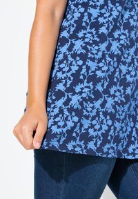 Top de tejido azul marino con un patrón floral en azul claro, con escote redondeado y mangas cortas. Combinado con jeans oscuros.