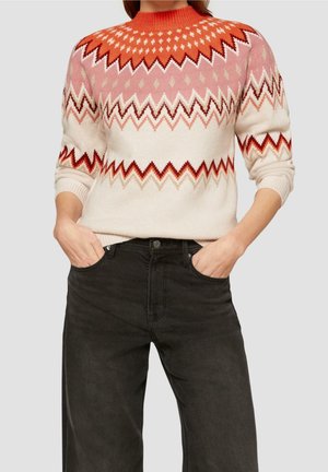 Stickad tröja med orange, rosa och krämfärgade zigzag-mönster. Rundad halsringning och ribbade ärmslut. Kombinerad med svarta vida jeans.