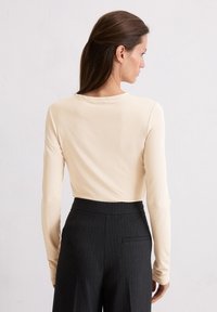 Langarm beige top met een ronde halslijn, gecombineerd met hoogsluitende zwarte gestreepte broek met een achterzakdetail.