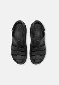 Sandales noires en plastique moulé, avec un design tressé, une texture lisse et une semelle intérieure rembourrée pour le confort.