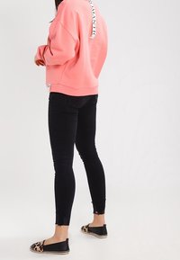 Sudadera rosa de gran tamaño con la etiqueta "ROMÁNTICO" en la parte de atrás, jeans skinny negros desgastados y zapatos de slip-on negros con estampado de leopardo.