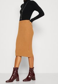 Jupe midi en tricot côtelé beige avec une taille ajustée, associée à un haut noir à manches longues et des bottines bordeaux à talons épais.