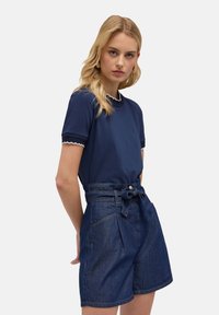 Camiseta navy con borde festoneado combinada con pantalones cortos de denim de tiro alto y cinturón, que presentan una textura suave y un ajuste estructurado.