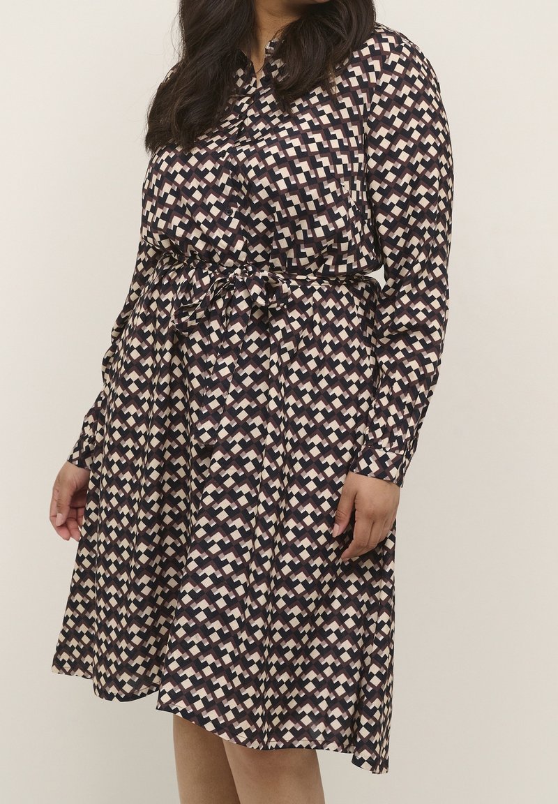 Robe à manches longues en bleu marine avec un motif géométrique en crème et rose pâle. Présente une taille ceinturée et une jupe évasée pour un ajustement décontracté.