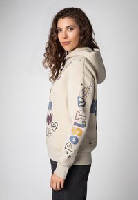 Lichtbeige hoodie met grafische ontwerpen, waaronder harten en bloemen in verschillende kleuren, geribde manchetten en een voorzak.