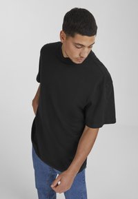 Svart bomull T-skjorte med avslappet passform, kort ermer og rund hals, kombinert med blå denimbukser. Enkelt design, uten mønstre eller aksenter.