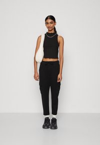 Crni rebrasti crop top s valovitim rubom, uparen s crnim cargo hlačama sa bočnim džepovima i strukom na vezanje, te crnim tenisicama.