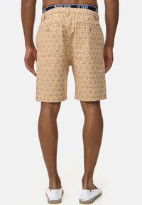 Shorts beige con un diseño geométrico. Presenta una cinturilla elástica con una etiqueta azul marino, dos bolsillos traseros y un corte relajado.