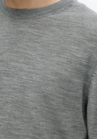 Γκρίζα ζακέτα με στρογγυλή λαιμόκοψη, μαλακή υφή και ελαφρώς υφασμένη διάκοσμο. Το ύφασμα φαίνεται ελαφρύ και άνετο.