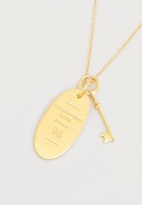 Χρυσό μενταγιόν ξενοδοχειακού κλειδιού με οβάλ πλακέτα χαραγμένη με το κείμενο "COMMON LANES HOTEL ROOM N: 98" και ένα κλειδί σε vintage στιλ σε χρυσή αλυσίδα.