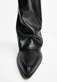 Botte de cheville en cuir noir avec un bout pointu et un design froncé. Texture lisse, style minimaliste, sans quincaillerie ni embellissements visibles.