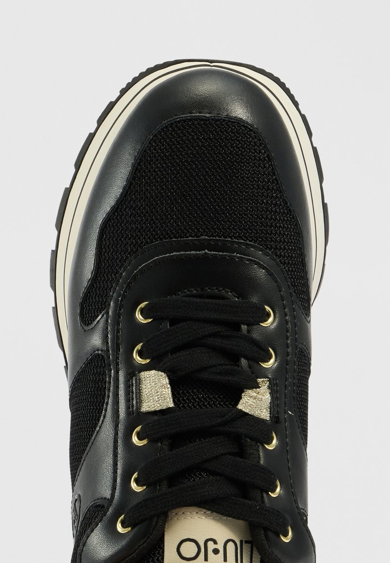 Schwarze Sneakers aus Netzgewebe und Lederakzenten. Ausgestattet mit goldenen Ösen, schwarzen Schnürsenkeln und einer strukturierten Sohle mit weißem Rand.