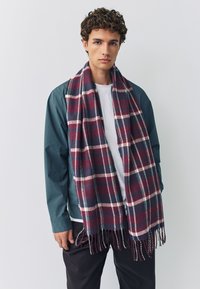 Sciarpa a quadri in bordeaux, blu navy e bianco, realizzata in tessuto morbido. Presenta estremità sfrangiate ed è drappeggiata intorno al collo del modello.