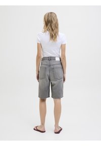 Harmaat farkkushortsit, joissa on löysä malli, taustataskut ja siisti vyötärö. Yhdistetty tiukkaan valkoiseen t-paitaan ja flip-flop-kenkiin.