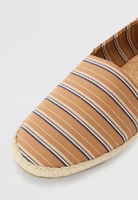 Espadrille i brunt stof med tynde vertikale striber i creme og marineblå, med en sål af jute reb og korkindsats.