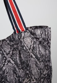 Tote bag met een gestructureerde zwart-grijze slangenprint. Voorzien van een dikke marineblauwe schouderband met rode en witte strepen. Eenvoudig, functioneel ontwerp.