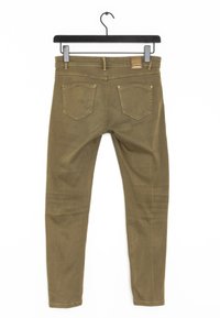 Jeans de corte ajustado en color verde oliva colgados de una percha negra. Incluye características como un cierre de cremallera, diseño de cinco bolsillos y un parche de cuero en la cintura.