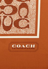 Tela marrón con un diseño estampado de letras entrelazadas y una etiqueta que dice "COACH LEATHERWARE" en letras blancas.