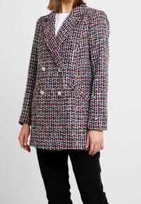 Blazer en tweed à double boutonnage présentant un motif de couleurs rouge, blanc et bleu, avec des boutons métalliques et un col structuré ; surface texturée.