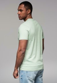 T-shirt verde menta a maniche corte realizzato in un tessuto morbido, dalla vestibilità aderente. Indossato con jeans in denim azzurro chiaro, che presentano uno stile casual e rilassato.