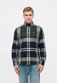 Kockás ing zöld, sötétkék és szürke színekben; gombos gallér; mellzseb; és hosszú ujjú. Az anyag textúrált és szövetes hatású.