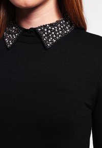 Top nero a costine con colletto impreziosito da strass trasparenti e scuri, che aggiungono consistenza e dettagli al design.