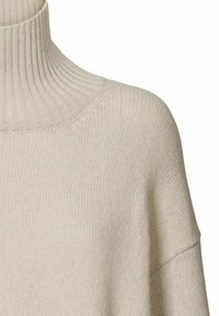 Beige geribbelde gebreide coltrui met een verlengde schoudernaad en fijne gebreide structuur op een witte achtergrond.