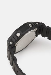 Montre en résine noire avec un boîtier rectangulaire épais, quincaillerie en argent, bracelet texturé et dos en acier inoxydable poli.