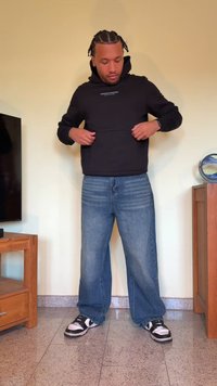 Sweatshirt preto com capuz e bolso frontal, usado com jeans azuis largos e ténis preto e branco; design minimalista, ajuste casual.