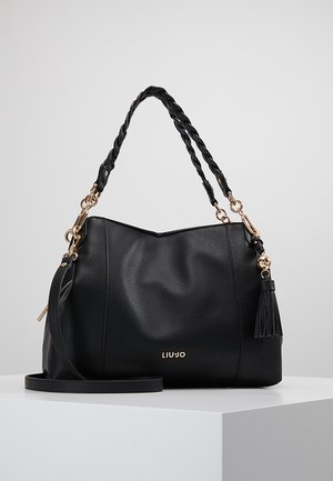 Czarna torebka z fakturowanej skóry z plecionym uchwytem, złotymi elementami, zawieszką w formie chwostu i logo "LIU JO" na froncie, spoczywająca na białym postumencie.