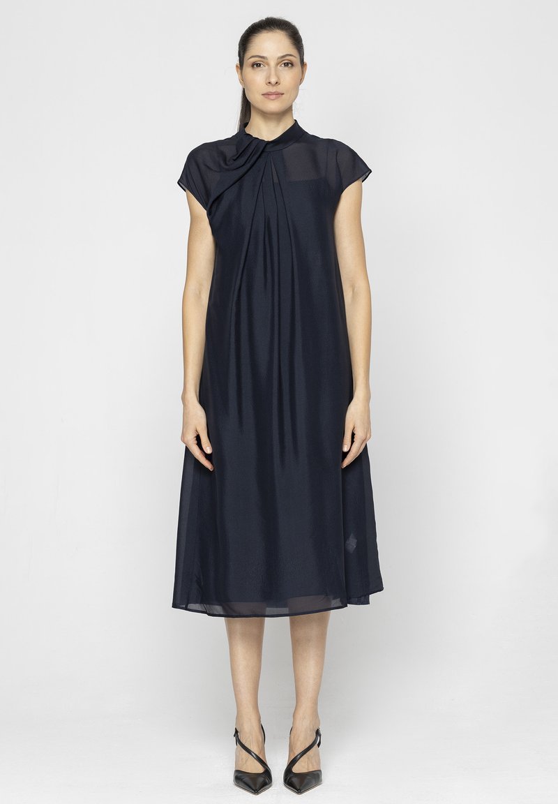 Granatowa midi sukienka z lekkiego materiału, z plisowanym dekoltem i rękawami typu cap. Połączona z czarnymi, szpiczastymi szpilkami.
