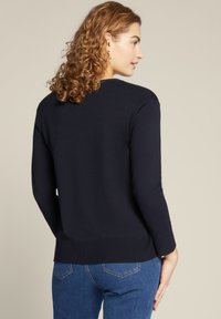 Donkerblauw gebreid sweater met geribde manchetten en zoom. Heeft een klassieke ronde halslijn en een gladde textuur. G gedragen met blauwe jeans.