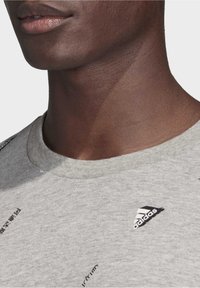 Szara bawełniana koszulka z okrągłym dekoltem, z czarnym nadrukowanym tekstem i małym czarnym logo Adidasa na lewej piersi.