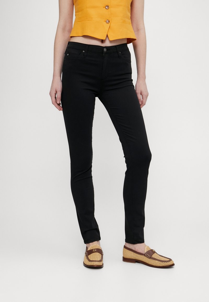 Jean noir ajusté avec une texture lisse, design à cinq poches et taille mi-haute. Associé à un haut court jaune et des chaussures tissées.