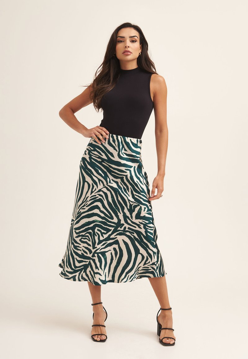Black sleeveless top paired with a green and white zebra-print satin skirt, featuring a flowing design and layered texture, complemented by black heels.