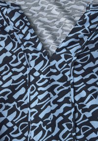 Kurzärmliges Oberteil mit einem blauen und schwarzen abstrakten Muster. Verfügt über einen V-Ausschnitt und einen weichen Stoff mit strukturierter Oberfläche.