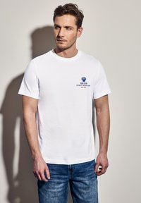 Bílý bavlněný tričko s grafickým motivem modré mušle a textem "BLUE CLAM FINEST SEAFOOD." Volný střih s krátkými rukávy.