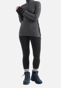 Chaqueta de cremallera de color gris oscuro, leggins negros ajustados y botas de senderismo azules con calcetines grises. La chaqueta tiene una textura acanalada y detalles en los paneles laterales.