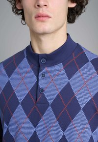 Polo a colletto di colore blu navy con un motivo a rombi in blu chiaro e rosso. Presenta tre bottoni al collo e un tessuto strutturato.