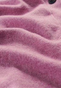 Zachte, textuurgebreide stof in lichtroze met zichtbare ribbels, met een knoopdetail dat zorgt voor zachte golven en diepte in het uiterlijk.