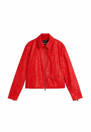 Punainen tekonahkatakki, jossa on lyhyt malli, terävä kaulus, vetoketjusuljenta edessä ja sivutasku, jossa on musta nepparikiinnike.