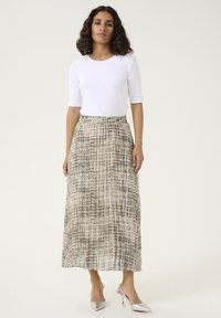 Falda maxi en beige con un patrón abstracto texturizado. Presenta una cintura elástica y se combina con una blusa blanca ajustada y tacones plateados.