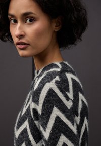 Pletený svetr v černé a bílé barvě se vzorem cikcak. Vyrobený z měkkého, texturovaného materiálu, s kulatým výstřihem a dlouhými rukávy.