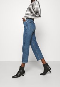 Blå denimhöga jeans med rak passform, avslutade med en rå kant. Kombinerat med svarta ankelstövlar med spetsig tå och kittenhæl.